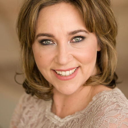 Christine Rice, a woman with shoulder-length light brown hair and green eyes, smiles warmly at the camera. She is wearing a lacy, cream-coloured top, and the background is softly blurred in neutral tones.