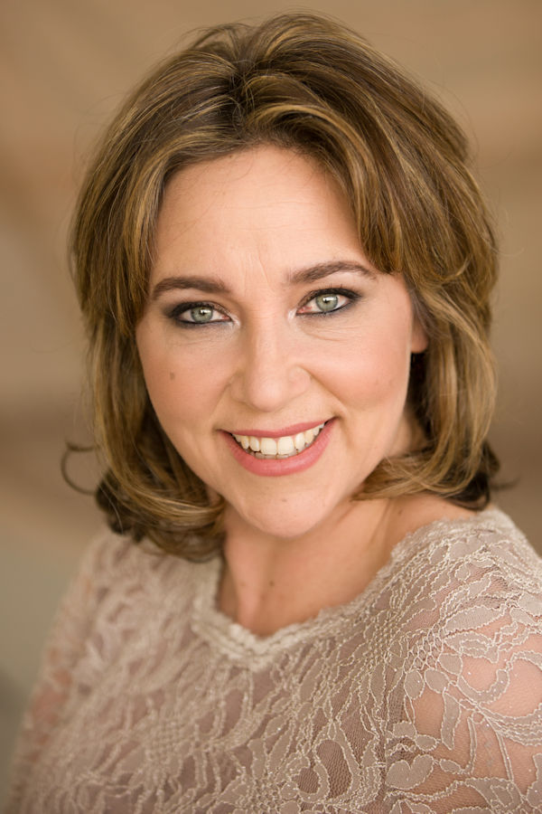 Christine Rice, a woman with shoulder-length light brown hair and green eyes, smiles warmly at the camera. She is wearing a lacy, cream-coloured top, and the background is softly blurred in neutral tones.