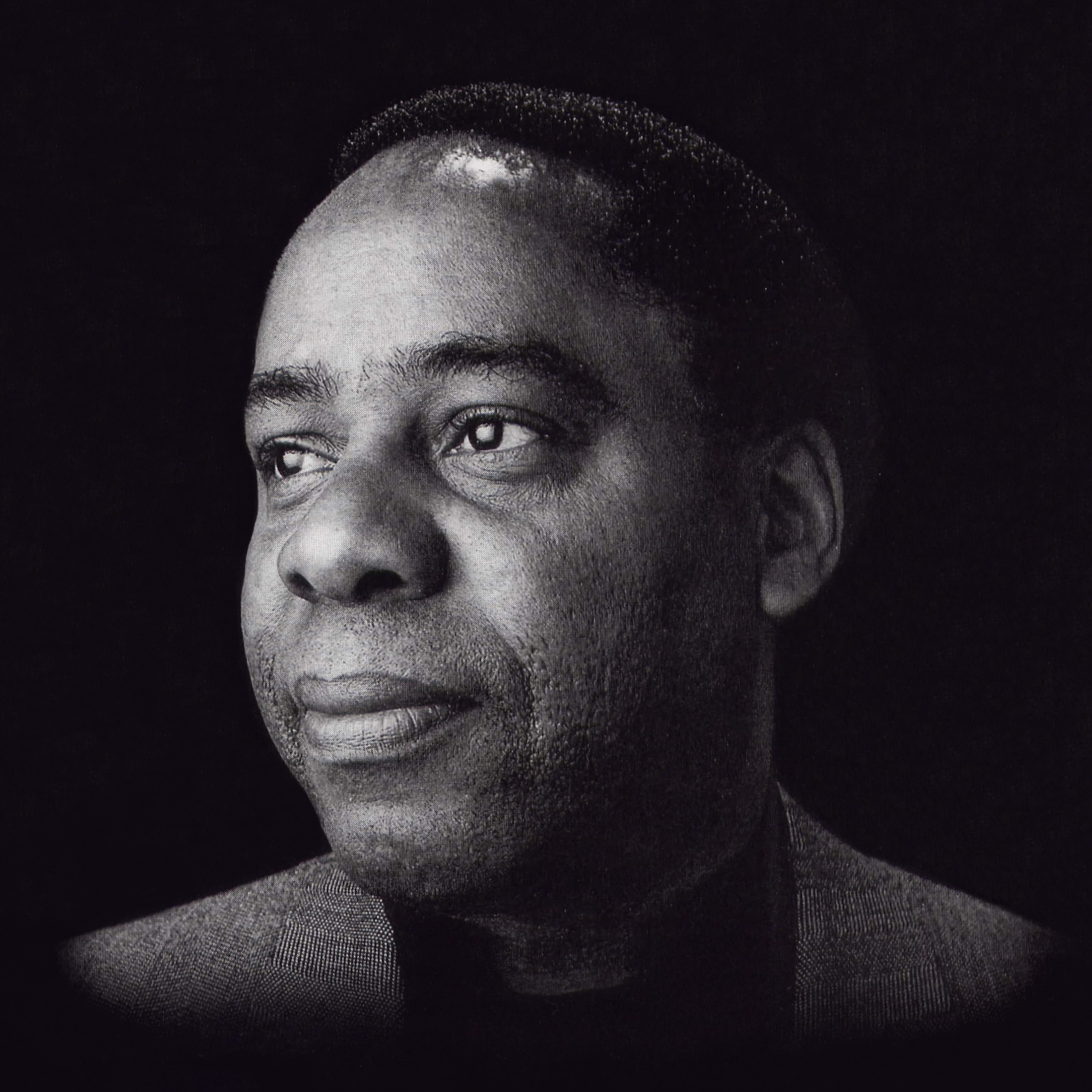 Black and white portrait of a man with short hair, wearing a suit jacket, looking slightly to the left with a calm, thoughtful expression—evoking the timeless style of George Gershwin—set against a dark background.