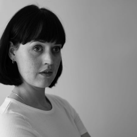 Bethan Langford, a woman with short dark hair and fringe, wearing a light-coloured shirt, looks off to the side with a thoughtful expression against a plain background. The image is in black and white.