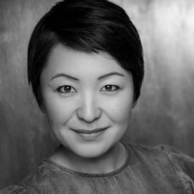 Black and white portrait of Haruka Kuroda, a woman with short dark hair, wearing a light-coloured top, smiling slightly, and looking directly at the camera against a softly blurred background.