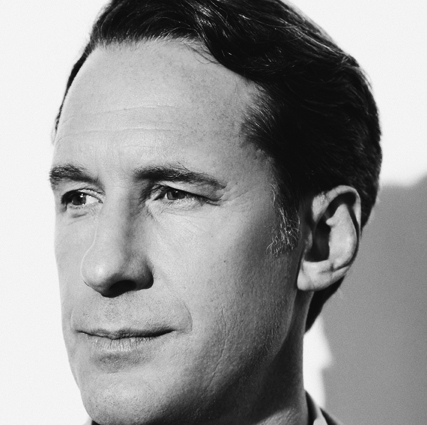 Black and white close-up portrait of baritone Jacques Imbrailo, an acclaimed opera singer. He gazes slightly to the left, with short dark hair and a calm, thoughtful expression. Shadowed lighting adds depth to the background.