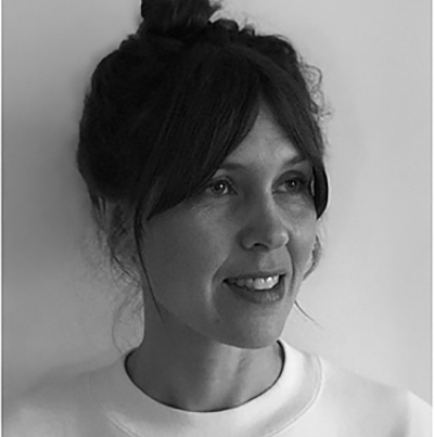 Black and white portrait of Sussie Juhlin-Wallén, a woman with dark hair in a loose bun, side-swept fringe, and a light-coloured top, looking slightly to the side and smiling softly against a plain background.