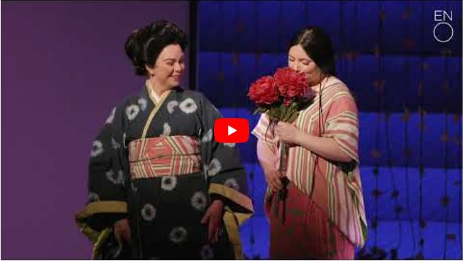 Two women in traditional Japanese kimonos stand together, evoking the grace of mothers in opera. One holds a bouquet of red flowers and smiles.
