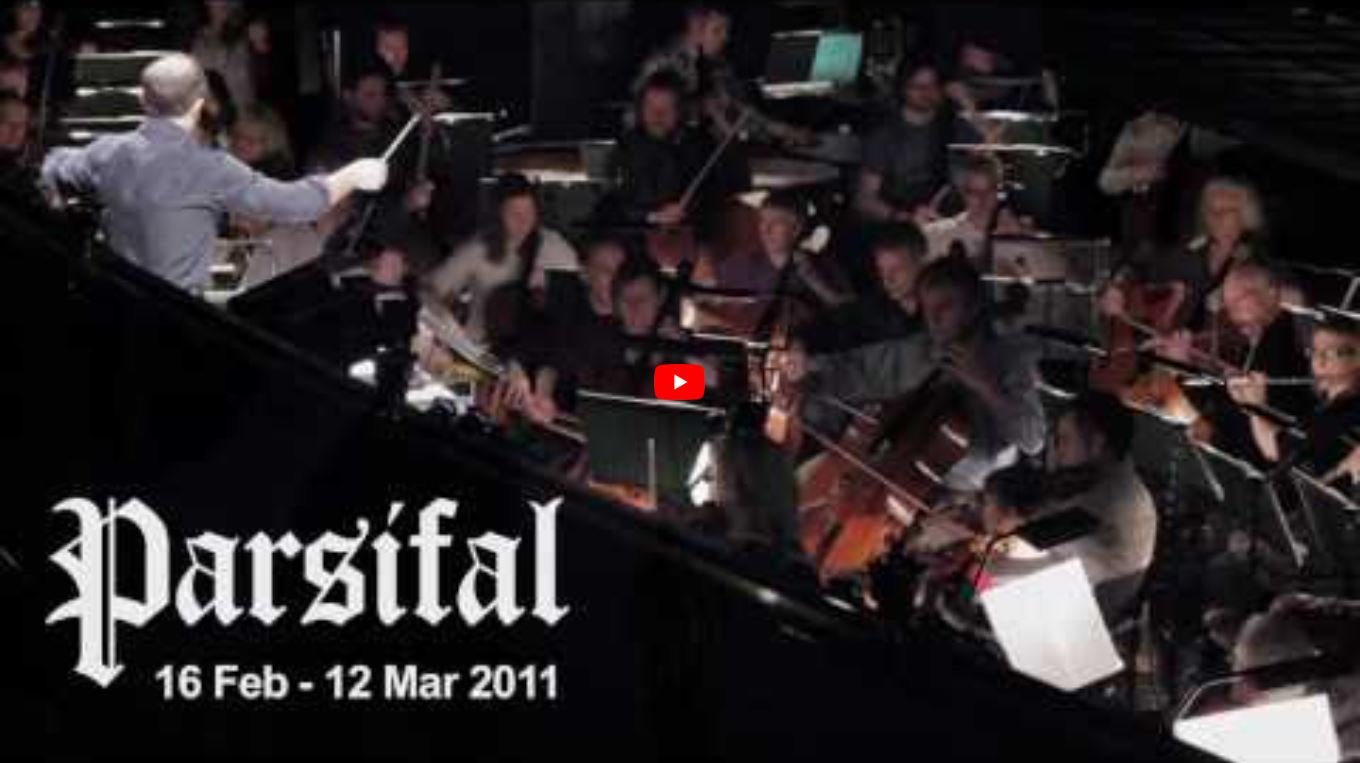 An orchestra performs with a conductor leading, surrounded by musicians.