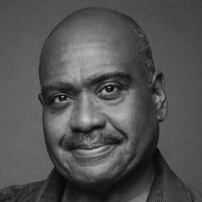 A middle-aged man with short hair and a moustache smiles gently at the camera in this black-and-white portrait. He is wearing a collared shirt and is positioned against a plain background.