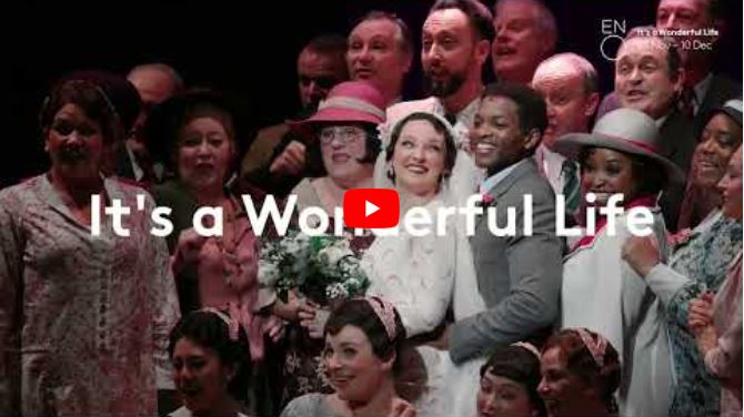 A large group of people dressed in vintage costumes smile and pose together on stage. Text overlay reads, It's a Wonderful Life, celebrating the classic story. A YouTube play button is centred.