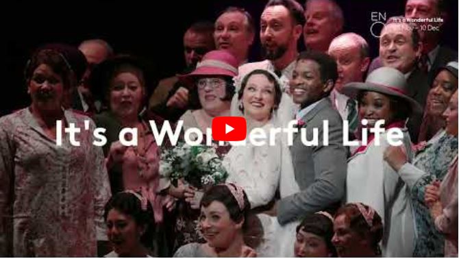 A joyful group of people in colourful costumes smile and pose together on stage, offering a lively introduction to It’s a Wonderful Life. White text reads, Its a Wonderful Life, with a red play button centred over the image.