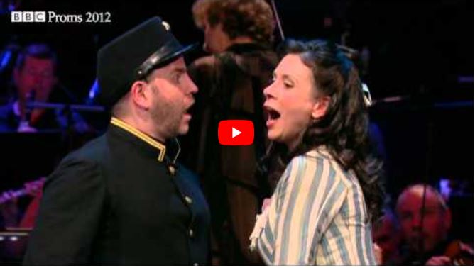 A man in a dark uniform and a woman in a striped dress are singing passionately on stage during a London BBC Proms 2012 performance