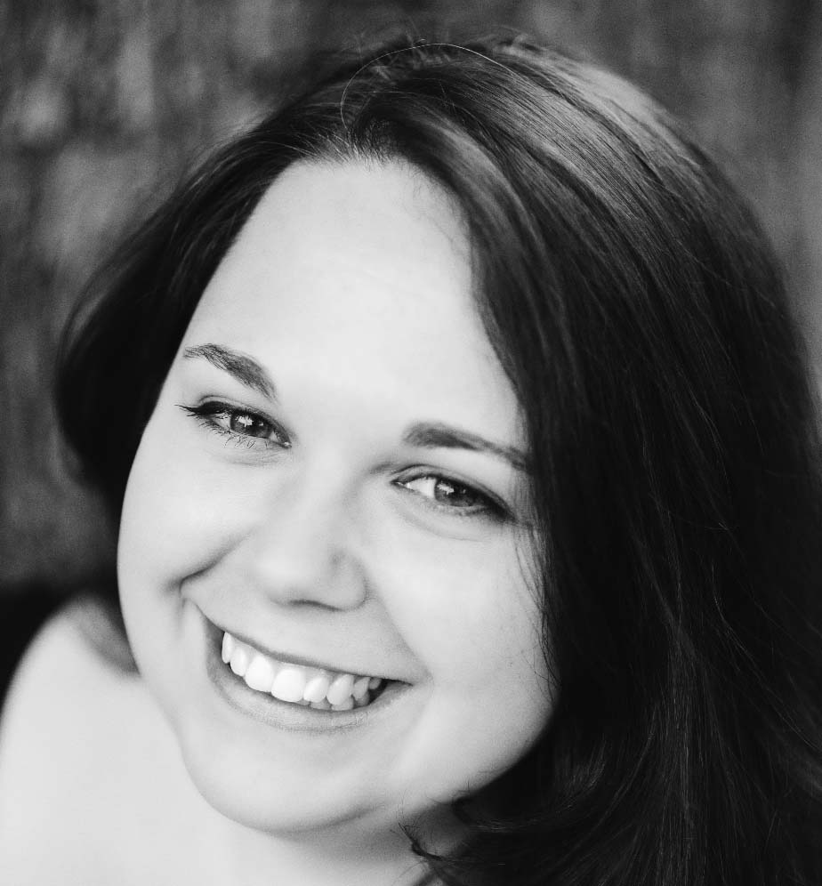 A black and white close-up photo of a smiling woman with straight, dark hair parted to the side, looking directly at the camera. The softly blurred background highlights her feature as one of the 2016 Harewood Artists.