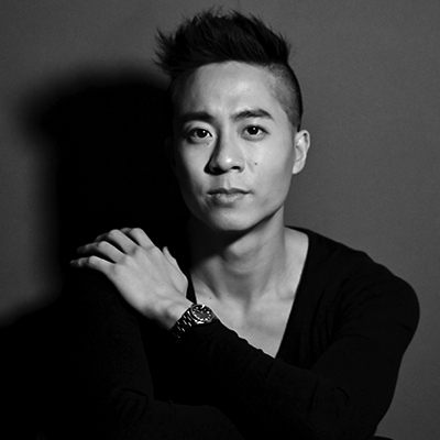 Image of Keith Pun with short, styled hair sits against a dark background, wearing a black long-sleeve shirt and a watch, with one arm crossed over their chest and a calm, serious expression.