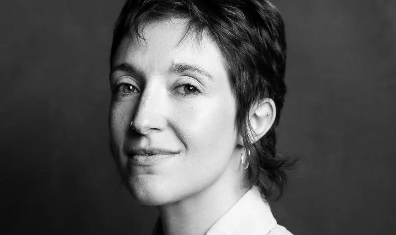 Black and white portrait of a Ruth Knight with short, dark hair, wearing a light-coloured collared shirt and hoop earrings, looking slightly to the side with a calm expression against a plain background.