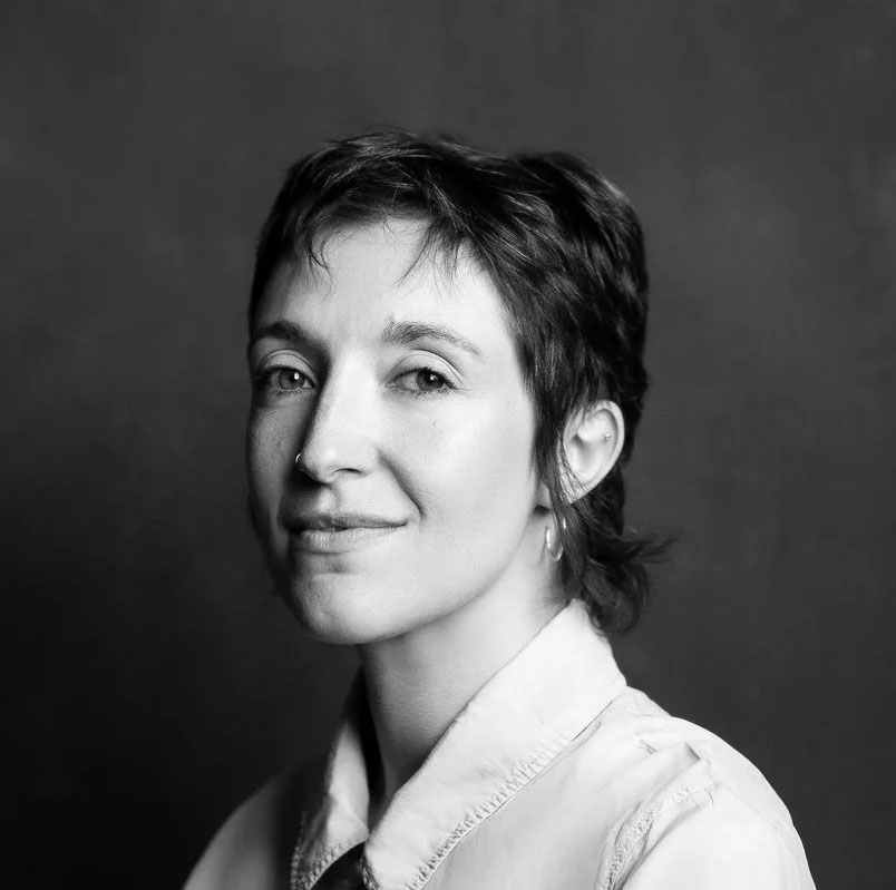 Black and white portrait of a Ruth Knight with short, dark hair, wearing a light-coloured collared shirt and hoop earrings, looking slightly to the side with a calm expression against a plain background.