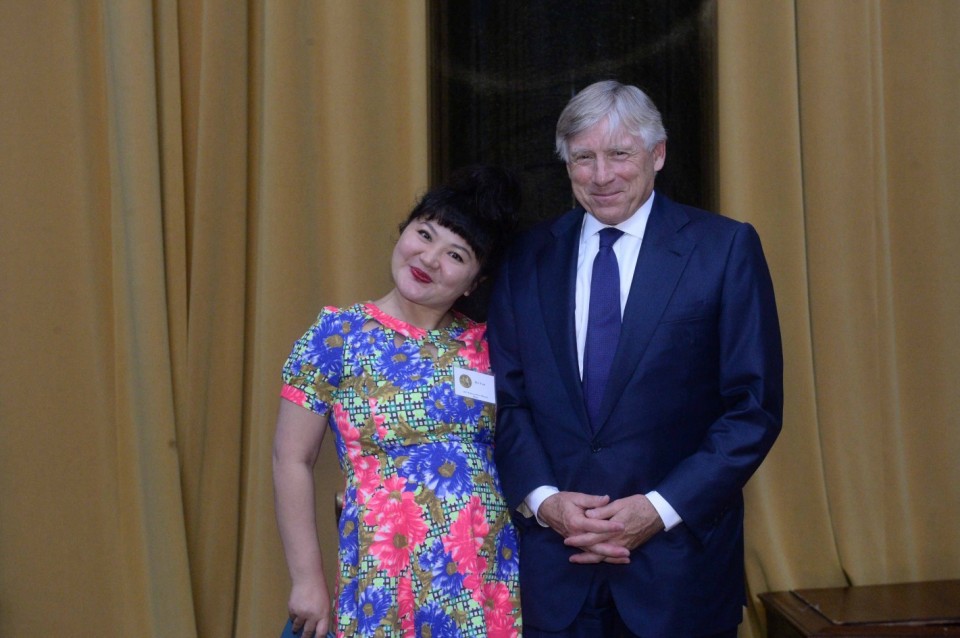 A woman in a colourful floral dress stands and smiles next to a man in a dark blue suit and tie, both posing for a photo.