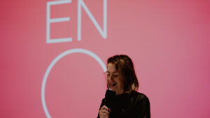 Annilese Miskimmon presents the 2026/27 season to assembled supporters, standing in front of a red screen with the ENO logo.
