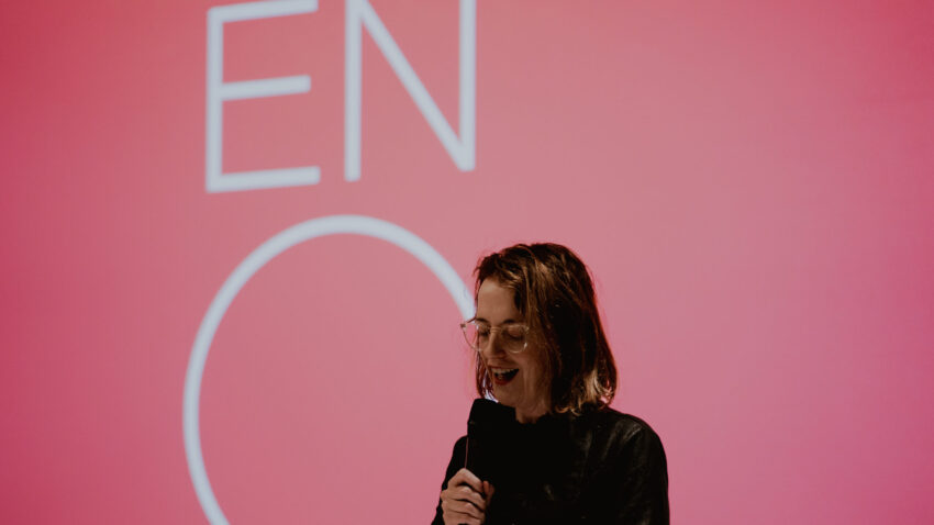 Annilese Miskimmon presents the 2026/27 season to assembled supporters, standing in front of a red screen with the ENO logo.