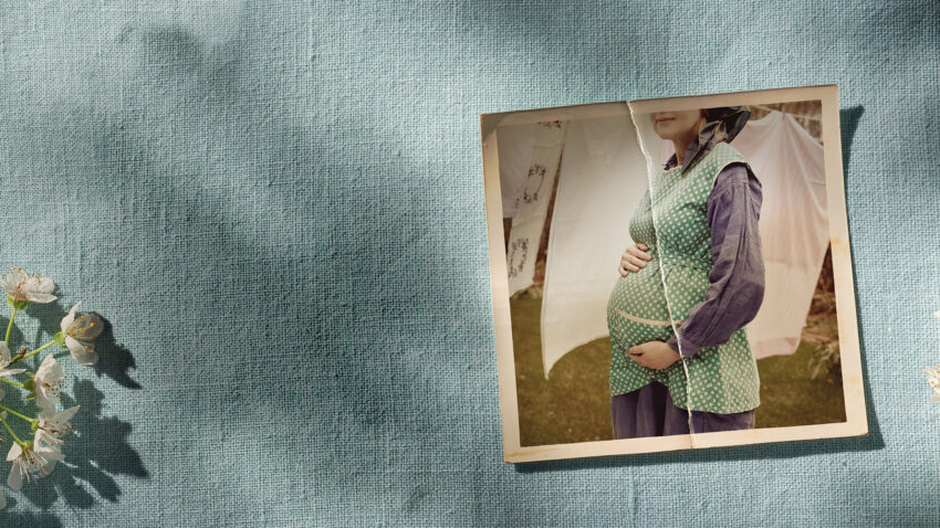A vintage photo of a pregnant woman holding her bump is placed on a textured blue fabric background with shadows and white flowers in the corner.
