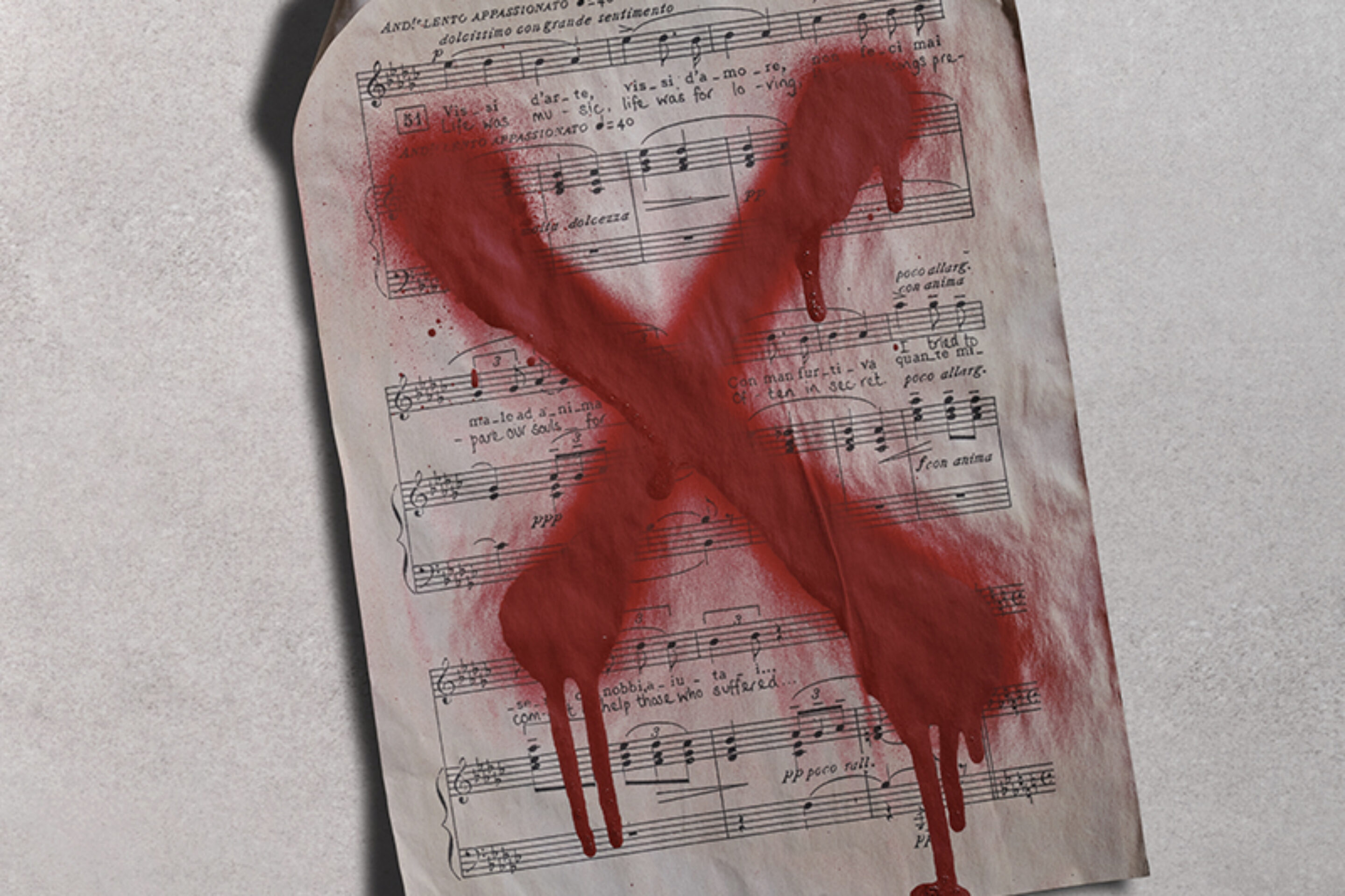 A sheet of music with Italian text is stained with a large, dripping red X painted across the page, symbolising rejection or censorship. The sheet is slightly creased and sits on a light surface.