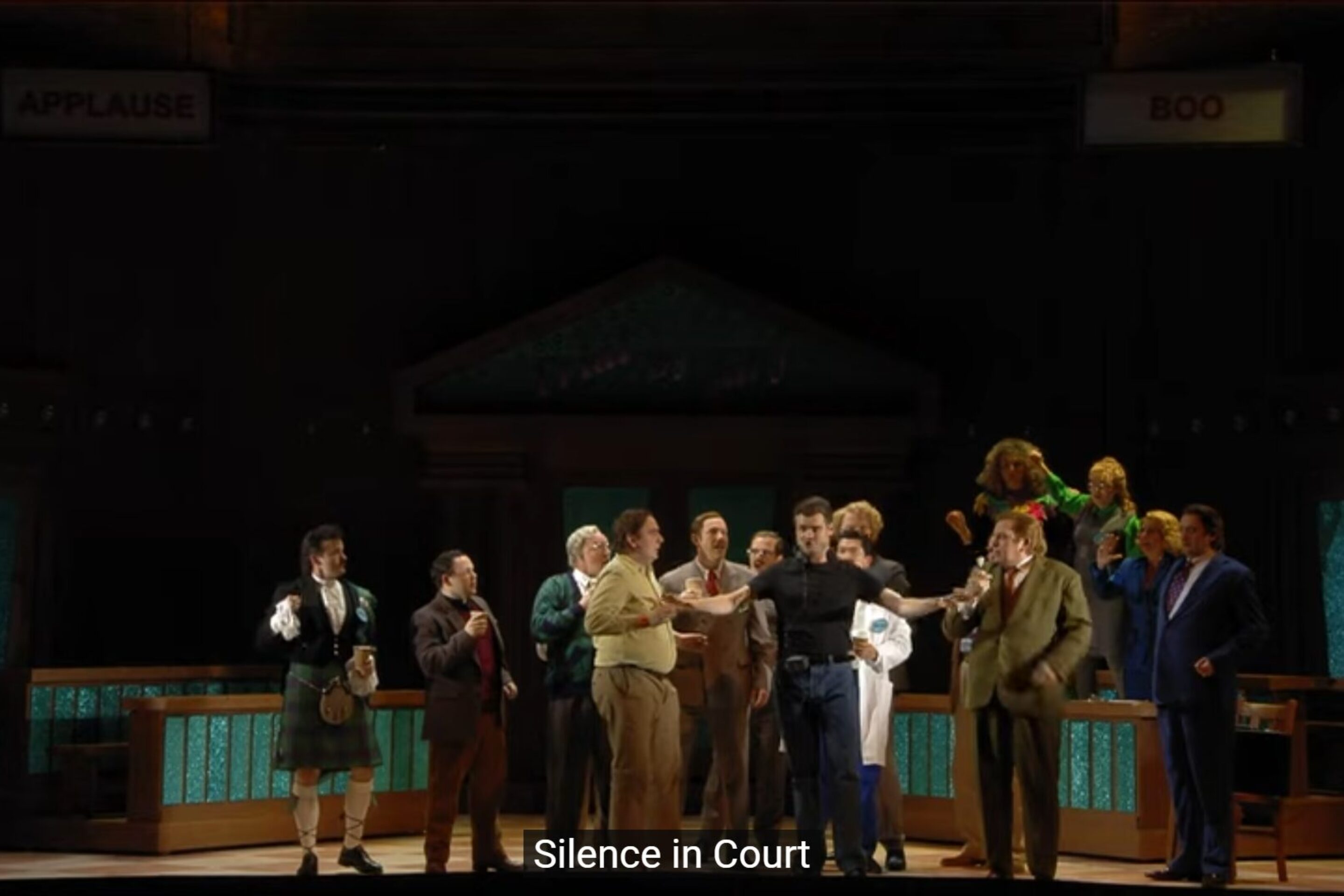 A theatre stage depicts a lively jury trial scene, with people in various costumes. Some stand, some gesture animatedly, as signs read “Applause” and “Boo.” The caption below states “Silence in Court,” setting the tone for an introduction to jury proceedings.