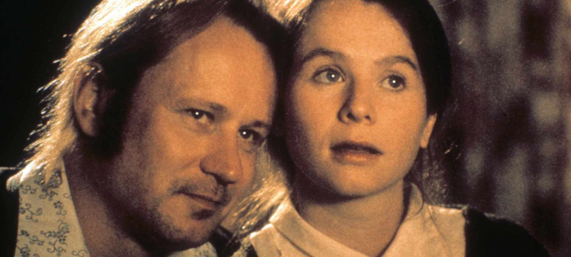 A man and a young girl sit closely together, both looking intently ahead. With an expressive, thoughtful look, the girl appears deep in thought, as if on the verge of an important introduction or breaking the waves of a new experience.