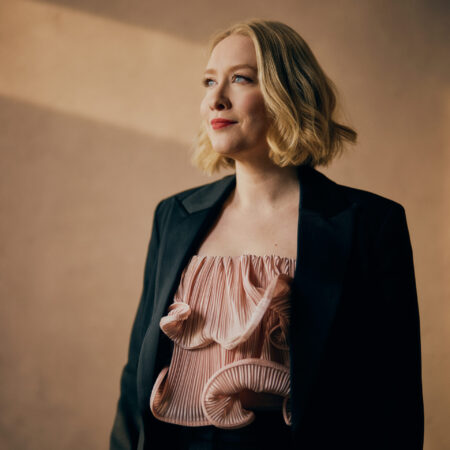 Sarah Gilforda with shoulder-length blonde hair, wearing a black blazer over a frilled pale pink top.