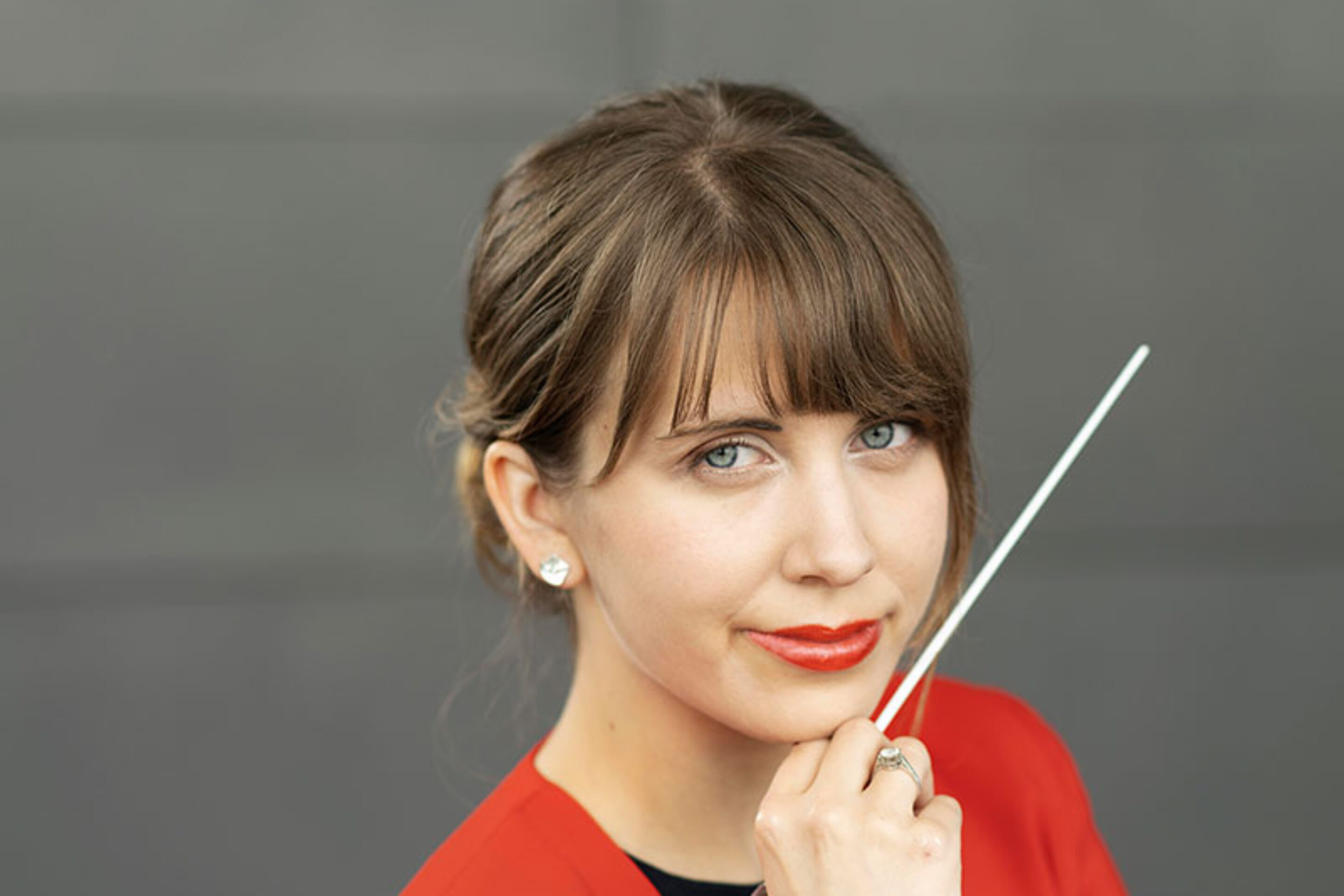 Conductor Aliisa Neige Barrière holding a baton near her chin.