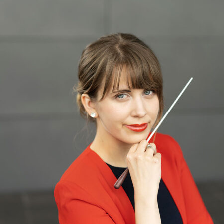 Conductor Aliisa Neige Barrière holding a baton near her chin.