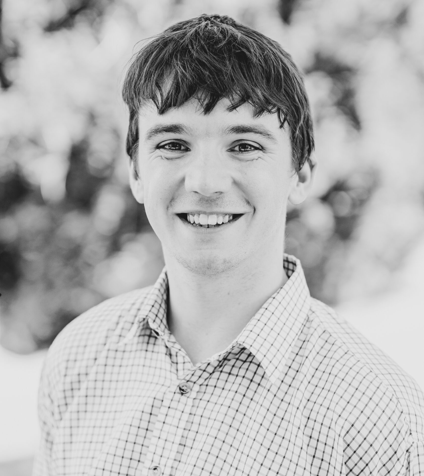 A black and white portrait of a young man smiling in a collared shirt.