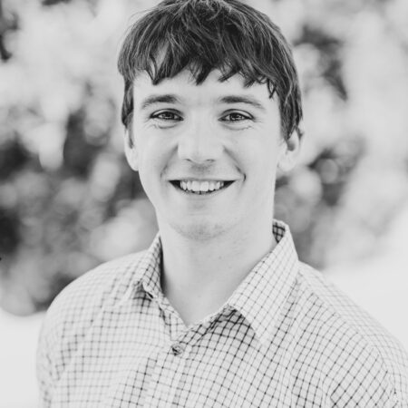 A black and white portrait of a young man smiling in a collared shirt.