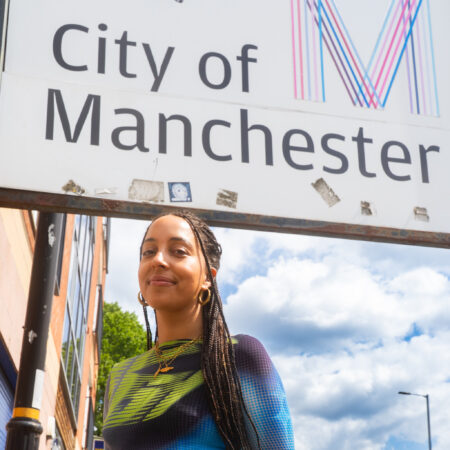 A person stands in front of a City of Manchester sign.