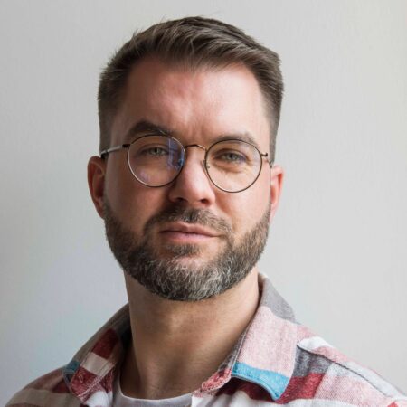 Composer Michael Betteridge, a man with a beard and round glasses wearing a checked shirt.
